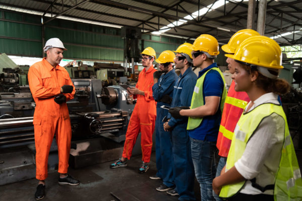 A foreman talking to a group of workers inside a machine shop