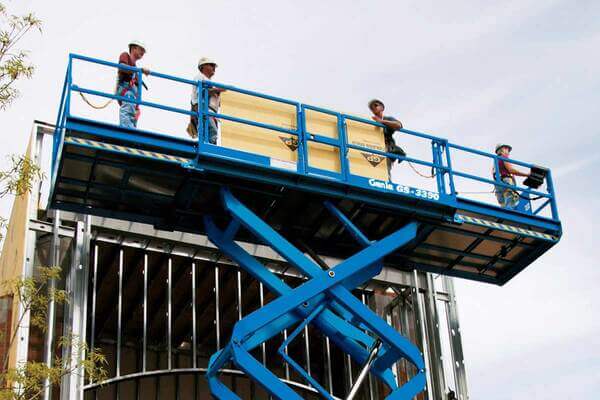 4 workers on a Genie scissor lift platform preparing a sheet of construction material