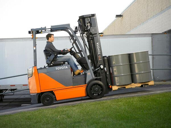 A Toyota forklift operator driving up an incline with a pallet of barrels on the forks