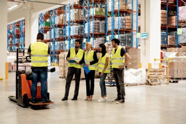 An instructor lecturing 4 forklift operator trainees in a warehouse