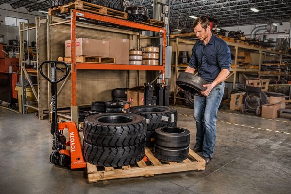 A warehouse worker loading forklift tires on a pallet